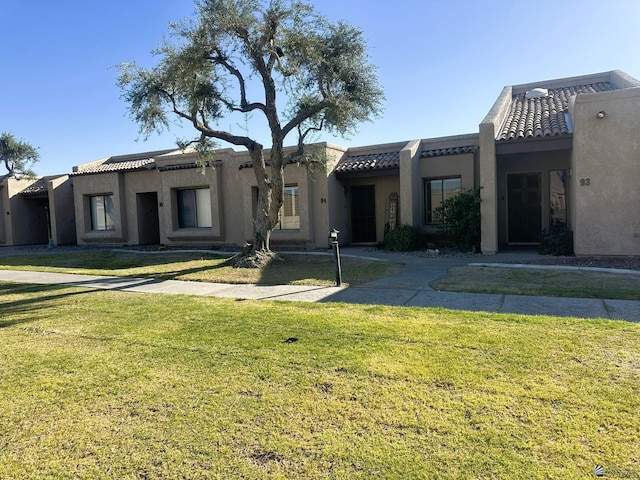 view of front facade with a front yard, a tile roof, and stucco siding