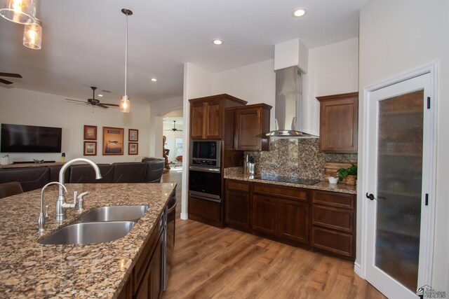 kitchen featuring sink, wall chimney exhaust hood, light stone countertops, black electric cooktop, and decorative light fixtures