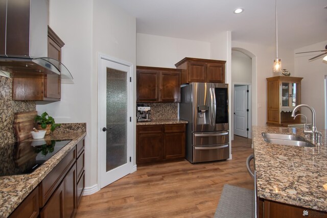 kitchen with wall chimney range hood, sink, stainless steel refrigerator with ice dispenser, decorative backsplash, and black electric cooktop