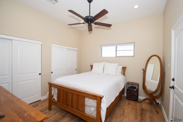 bedroom with wood-type flooring, ceiling fan, and multiple closets