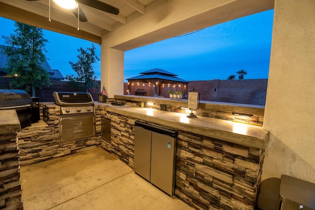 patio terrace at dusk with a gazebo, area for grilling, and exterior kitchen