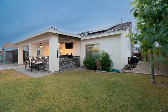 back house at dusk with an outdoor kitchen, ceiling fan, a yard, a bar, and a patio