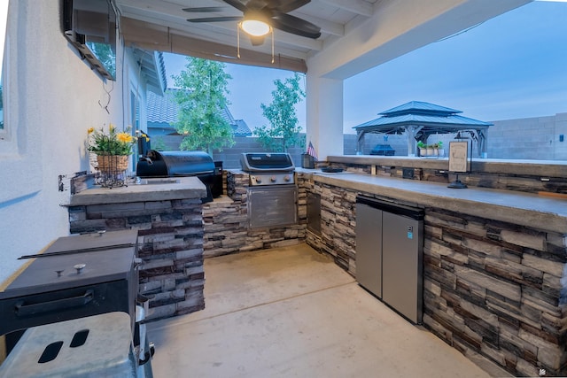 view of patio / terrace featuring a gazebo, ceiling fan, area for grilling, and exterior kitchen