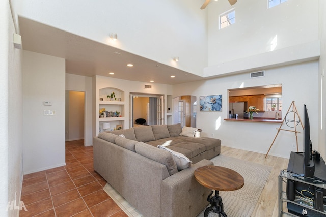 tiled living room with a towering ceiling, ceiling fan, and built in features