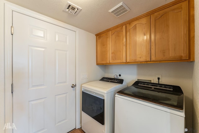 clothes washing area featuring a textured ceiling, cabinets, and washing machine and dryer