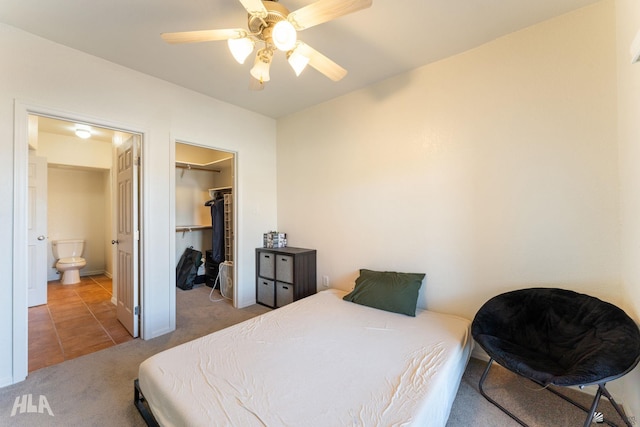 bedroom with ensuite bath, a closet, a walk in closet, ceiling fan, and light carpet