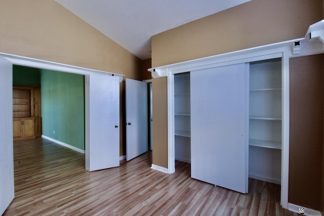 unfurnished bedroom featuring vaulted ceiling, a closet, and light wood-type flooring