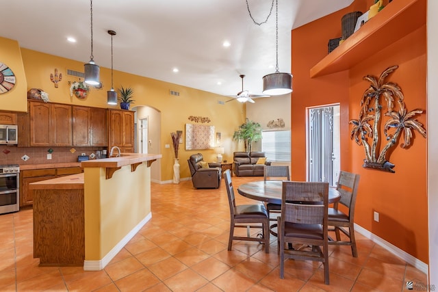 kitchen with ceiling fan, stainless steel appliances, decorative backsplash, a kitchen bar, and decorative light fixtures