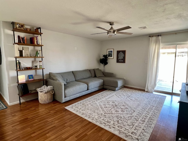 living room with a textured ceiling, ceiling fan, wood finished floors, visible vents, and baseboards