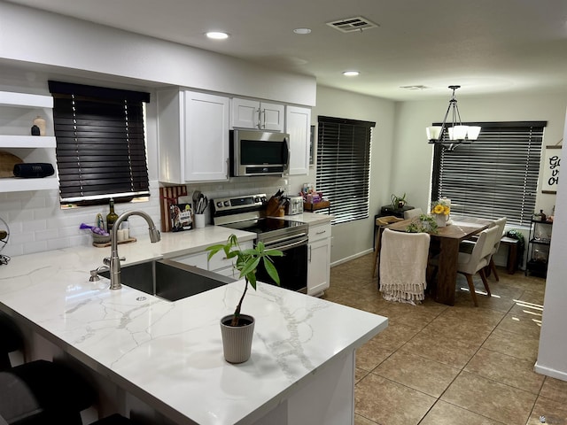 kitchen with light stone counters, visible vents, appliances with stainless steel finishes, a sink, and a peninsula