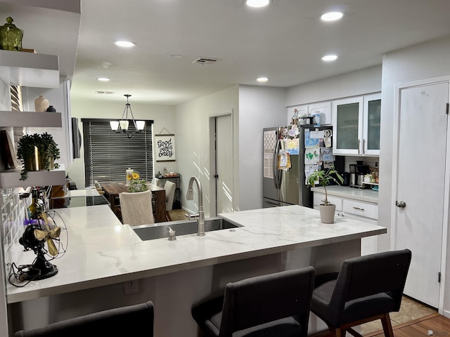 kitchen featuring glass insert cabinets, freestanding refrigerator, white cabinetry, a sink, and a kitchen bar