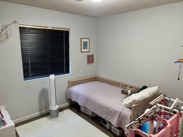 bedroom with baseboards, a textured ceiling, and wood finished floors