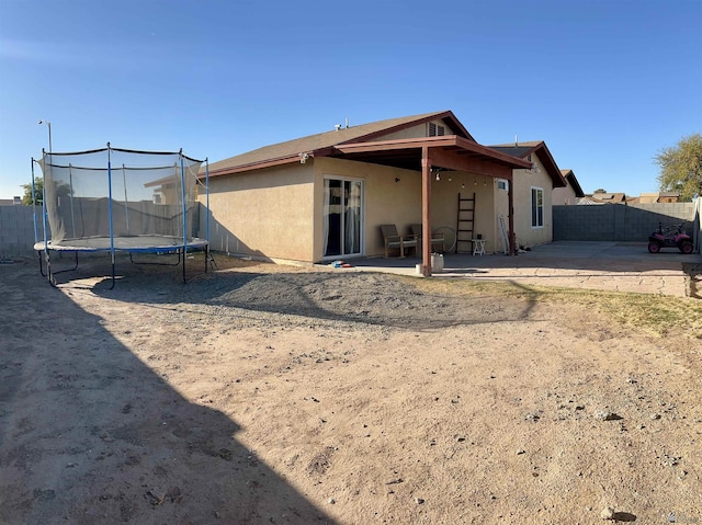 rear view of house featuring a patio, a trampoline, a fenced backyard, and stucco siding