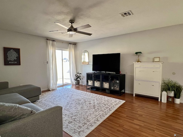 living area featuring ceiling fan, dark wood-style flooring, visible vents, and baseboards