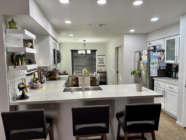 kitchen featuring a peninsula, white cabinetry, appliances with stainless steel finishes, open shelves, and a kitchen bar