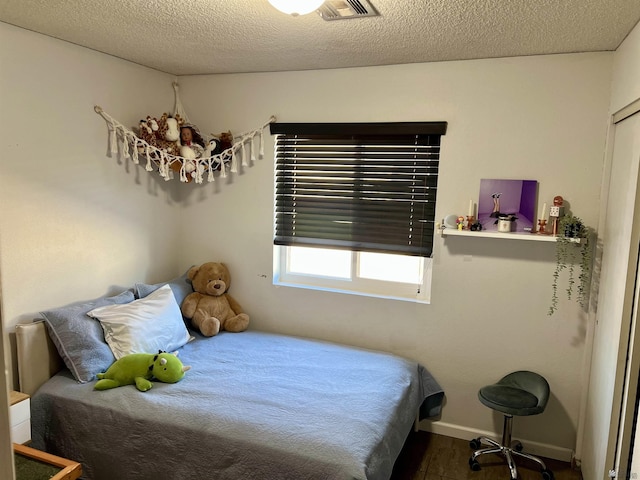 bedroom featuring visible vents, a textured ceiling, baseboards, and wood finished floors