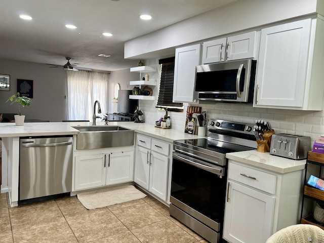 kitchen featuring a peninsula, a sink, appliances with stainless steel finishes, decorative backsplash, and open shelves