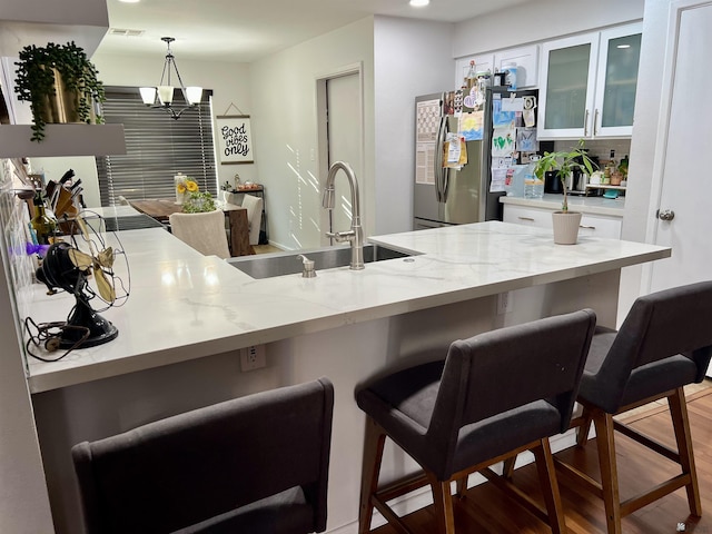 kitchen with white cabinets, a kitchen breakfast bar, a sink, and freestanding refrigerator