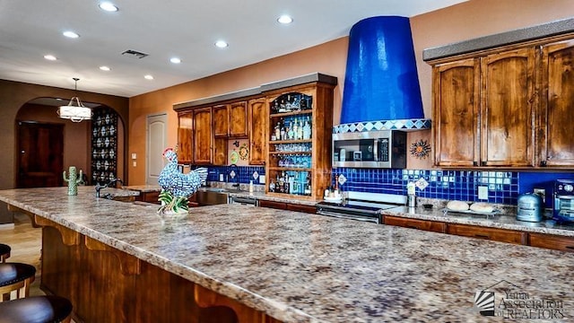 kitchen featuring light stone counters, arched walkways, appliances with stainless steel finishes, and a kitchen bar