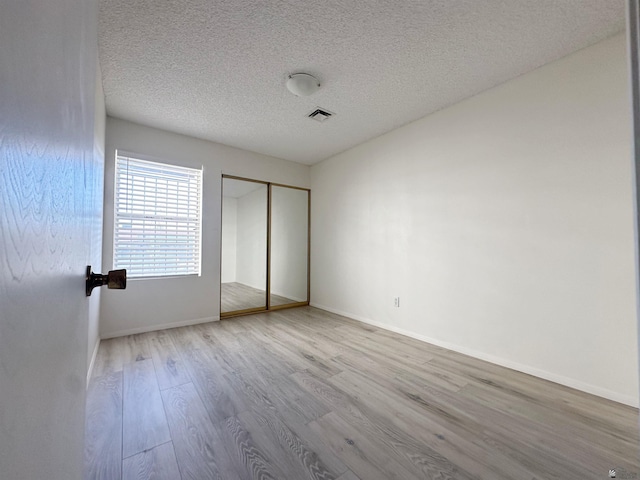 unfurnished bedroom with a closet, light hardwood / wood-style floors, and a textured ceiling