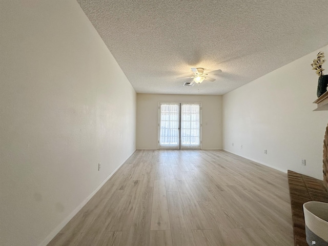 empty room with a fireplace, a textured ceiling, light hardwood / wood-style floors, and ceiling fan