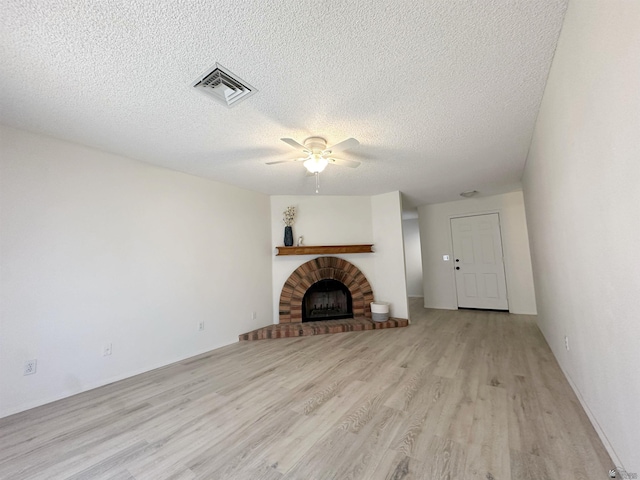 unfurnished living room featuring a fireplace, ceiling fan, light wood-type flooring, and a textured ceiling