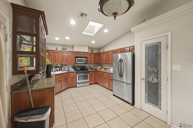 kitchen with dark stone countertops, appliances with stainless steel finishes, vaulted ceiling with skylight, sink, and light tile patterned flooring