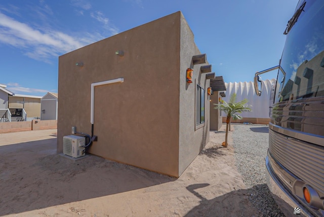 view of side of property featuring ac unit, stucco siding, and fence