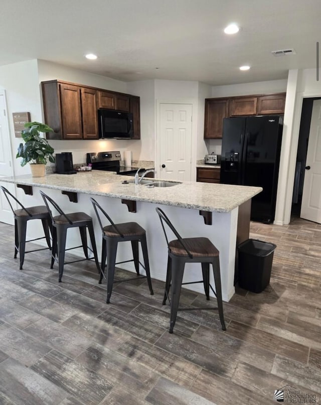 kitchen with a breakfast bar area, kitchen peninsula, dark brown cabinetry, and black appliances