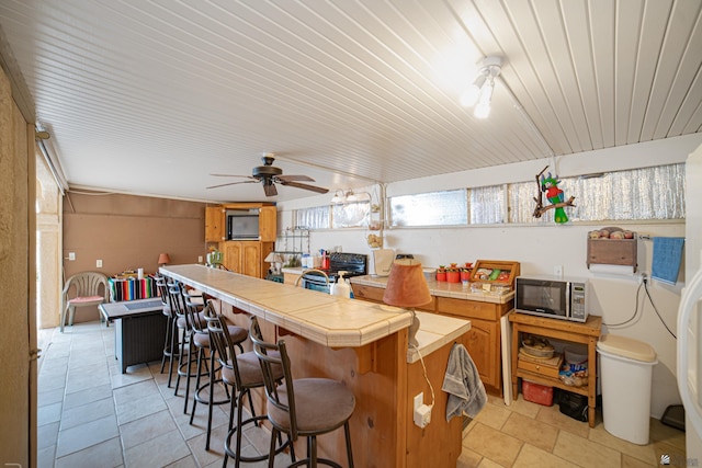 kitchen featuring ceiling fan, tile countertops, a breakfast bar, and light tile patterned floors