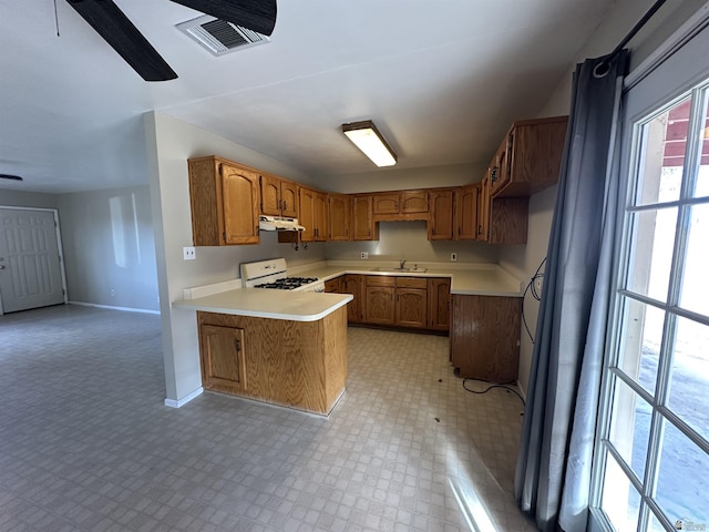 kitchen featuring gas range gas stove, light floors, light countertops, brown cabinets, and a peninsula