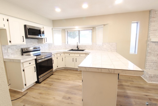 kitchen featuring kitchen peninsula, light hardwood / wood-style floors, white cabinets, appliances with stainless steel finishes, and sink