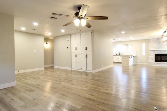 unfurnished living room featuring sink, a brick fireplace, light wood-type flooring, and ceiling fan