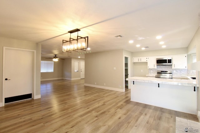 kitchen with kitchen peninsula, a breakfast bar, ceiling fan with notable chandelier, white cabinets, and appliances with stainless steel finishes