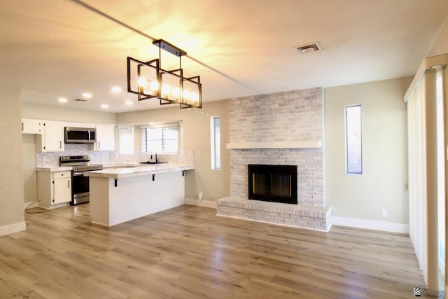 kitchen featuring stainless steel appliances, hanging light fixtures, kitchen peninsula, a kitchen bar, and white cabinetry