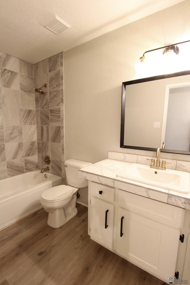 full bathroom with toilet, wood-type flooring, vanity, tiled shower / bath, and a textured ceiling