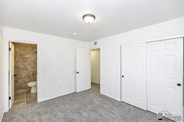 unfurnished bedroom featuring visible vents, ensuite bath, a textured ceiling, carpet floors, and a closet