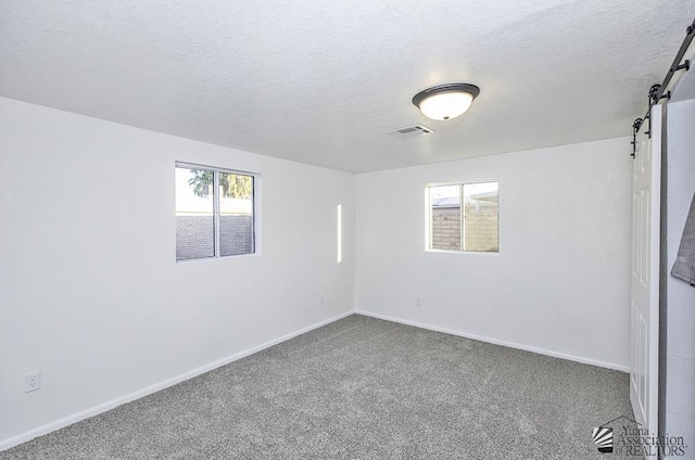 spare room with a barn door, baseboards, visible vents, a textured ceiling, and carpet flooring