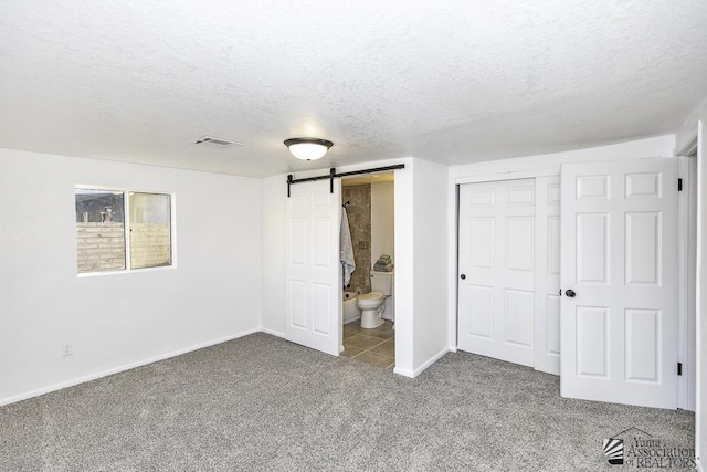 unfurnished bedroom featuring carpet, a closet, visible vents, a barn door, and a textured ceiling