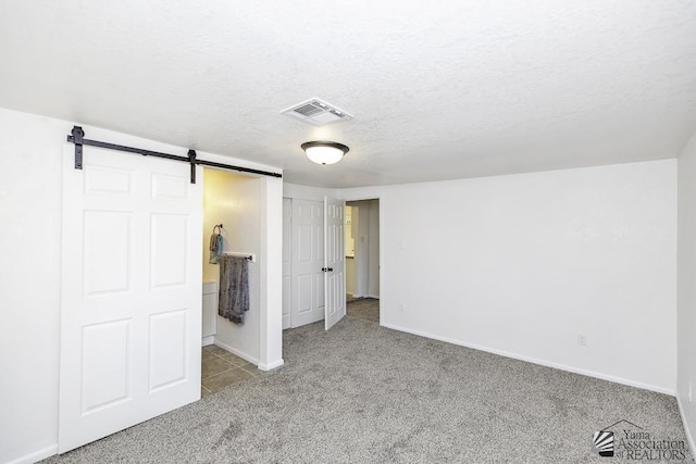 unfurnished bedroom featuring visible vents, a barn door, light carpet, a textured ceiling, and baseboards