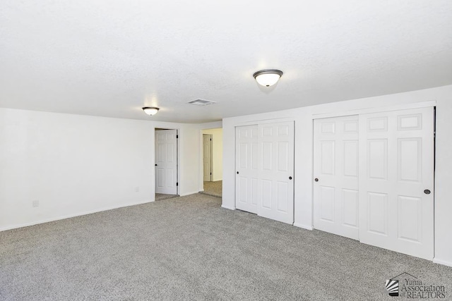 unfurnished bedroom with multiple closets, visible vents, carpet floors, and a textured ceiling