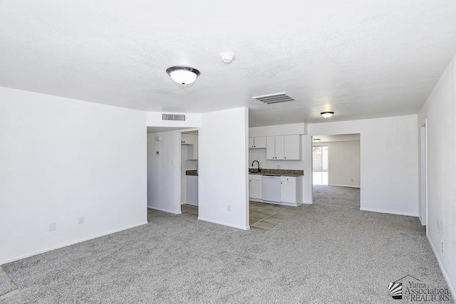 unfurnished living room featuring visible vents, a sink, light carpet, and a textured ceiling