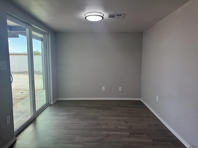 unfurnished room with visible vents, a textured ceiling, dark wood-type flooring, and baseboards