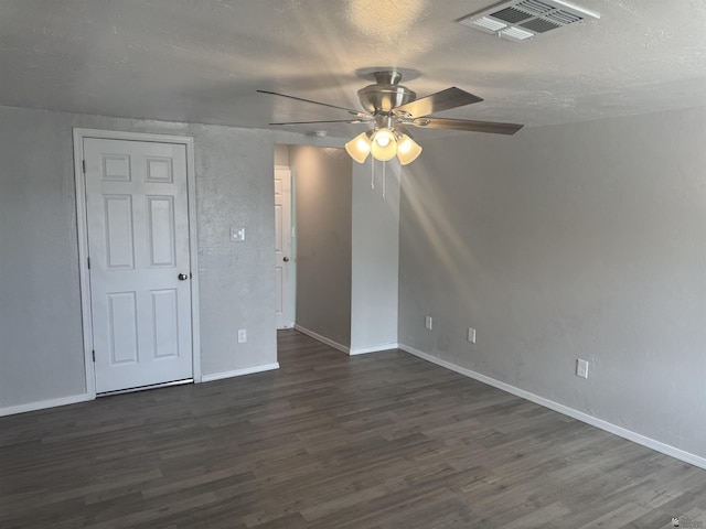 empty room featuring baseboards, dark wood-style floors, visible vents, and ceiling fan