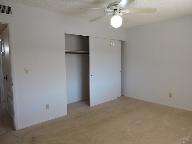 unfurnished bedroom featuring ceiling fan, light colored carpet, a closet, and a textured ceiling