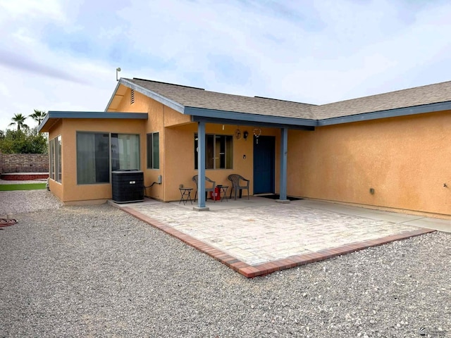 back of house with a patio, central AC unit, a shingled roof, and stucco siding