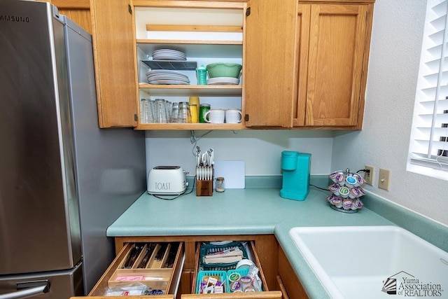 kitchen featuring a sink, brown cabinetry, light countertops, and freestanding refrigerator