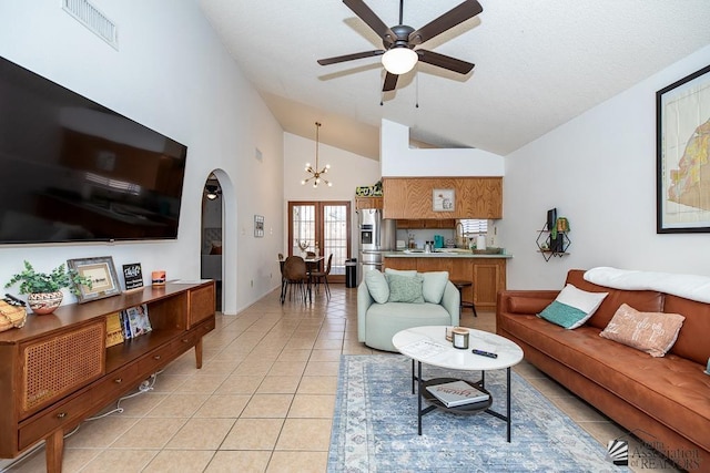 living area featuring visible vents, high vaulted ceiling, light tile patterned flooring, arched walkways, and ceiling fan with notable chandelier