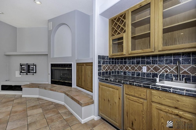 kitchen featuring a fireplace, light tile patterned floors, backsplash, and sink