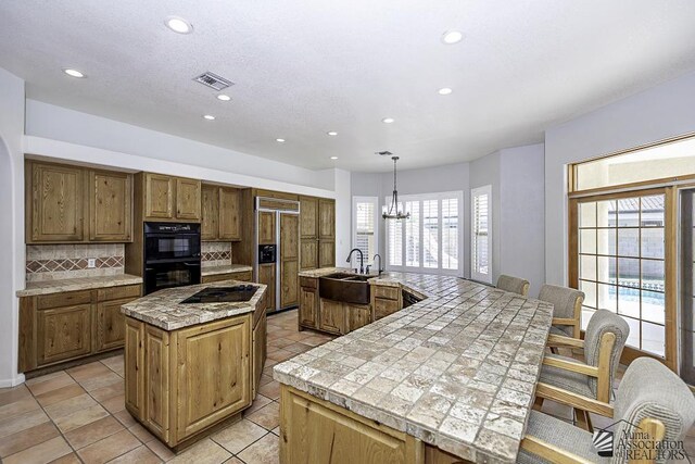 kitchen with sink, hanging light fixtures, double oven, an island with sink, and paneled built in fridge